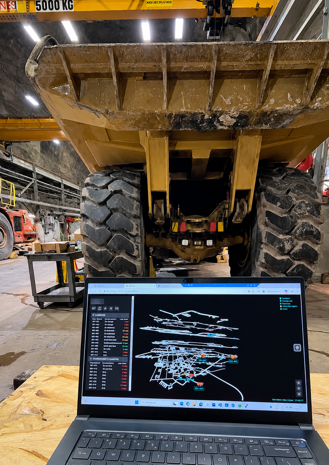 Ordinateur affichant une interface de suivi numérique devant un camion minier dans un atelier